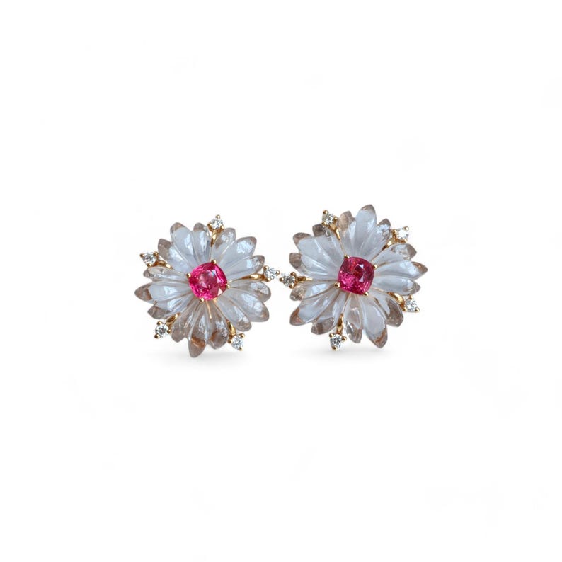 May include: A pair of gold earrings with a flower design. Each earring features a pink gemstone in the center surrounded by clear stones.