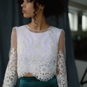May include: A white lace top with a sheer overlay and a green satin skirt. The top features a floral design and the skirt is a simple, elegant style.