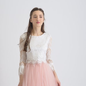 Puede incluir: Una mujer con un top de encaje blanco y una falda de tul rosa. El top tiene un escote redondo y mangas tres cuartos. La falda es amplia y fluida.