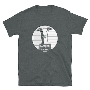 May include: Dark grey t-shirt featuring a white graphic of a dog's head inside a circle with horizontal lines. The dog has a sign that reads "PARTNER IN CRIME". The shirt is made of a soft material.