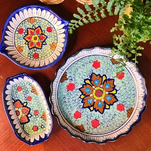 May include: Three Talavera pottery dishes with blue and white borders and colourful floral designs. The dishes are on a wooden surface with two candle holders.