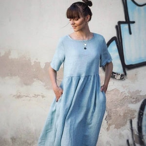 May include: A light blue linen dress with short sleeves and a gathered skirt. The dress has pockets on both sides.