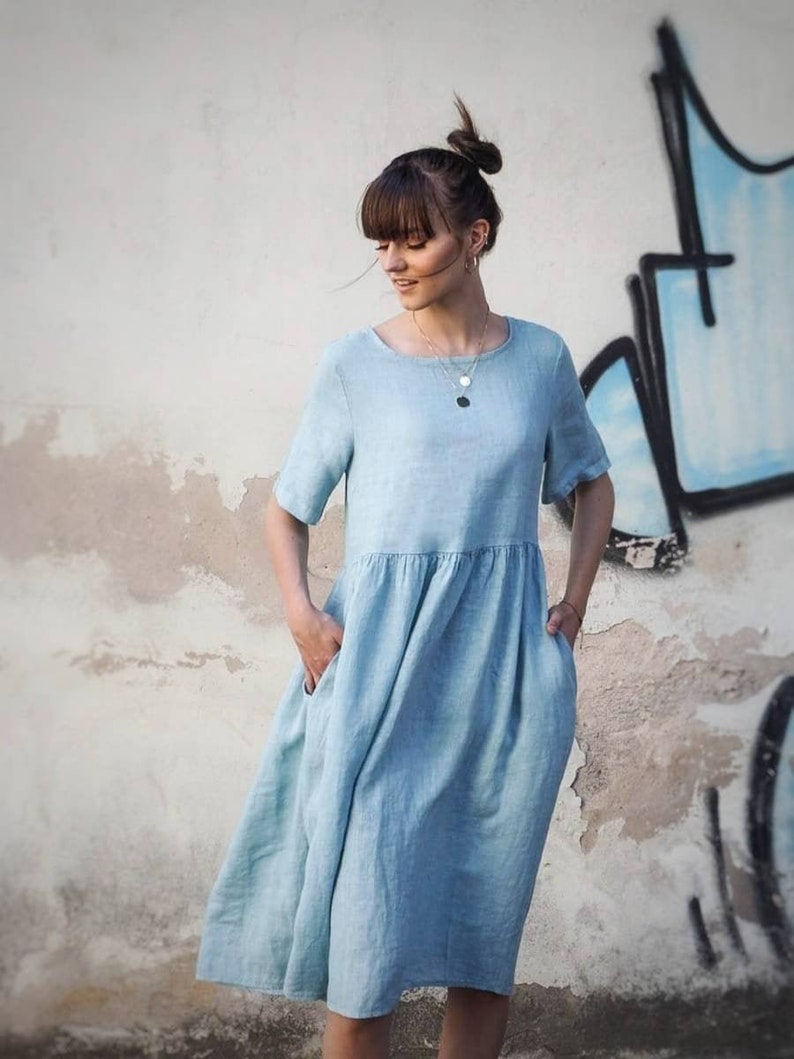 May include: A light blue linen dress with short sleeves and a gathered skirt. The dress has pockets on both sides.