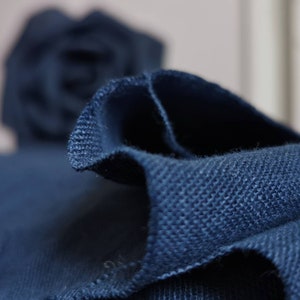 May include: Close-up of a dark blue fabric with a textured weave. The fabric is folded and the edges are frayed.