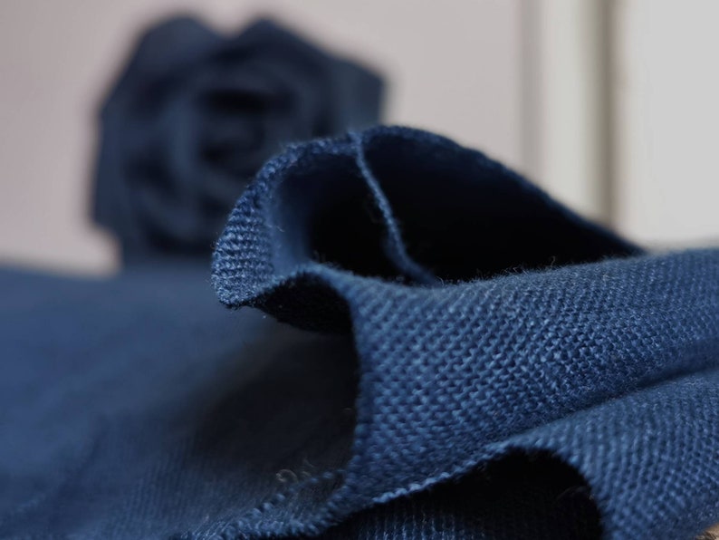 May include: Close-up of a dark blue fabric with a textured weave. The fabric is folded and the edges are frayed.