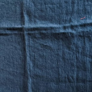 May include: A close-up of a dark blue fabric with a textured surface. The fabric is folded in half, creating a crease down the center.
