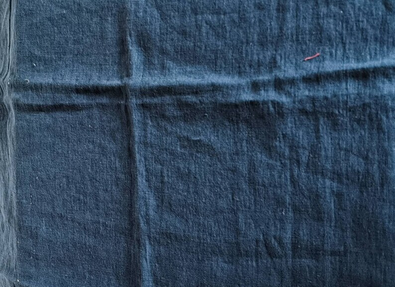 May include: A close-up of a dark blue fabric with a textured surface. The fabric is folded in half, creating a crease down the center.