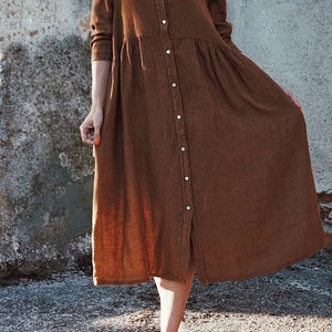 May include: A long-sleeved brown linen shirt dress with a button-up front and a slightly gathered skirt.