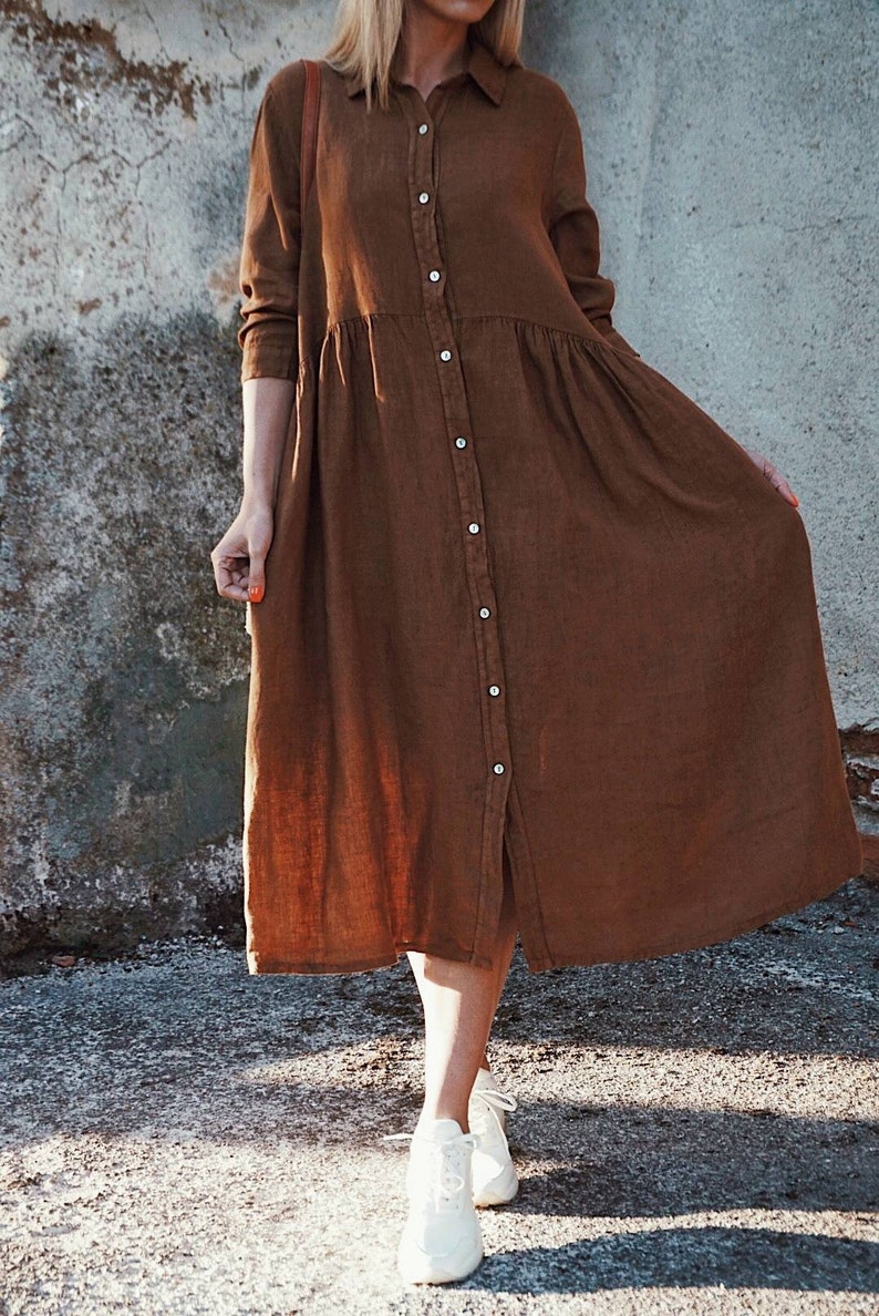 May include: A long-sleeved brown linen shirt dress with a button-up front and a slightly gathered skirt.