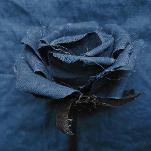 May include: A blue fabric rose with frayed edges, against a blue fabric background.