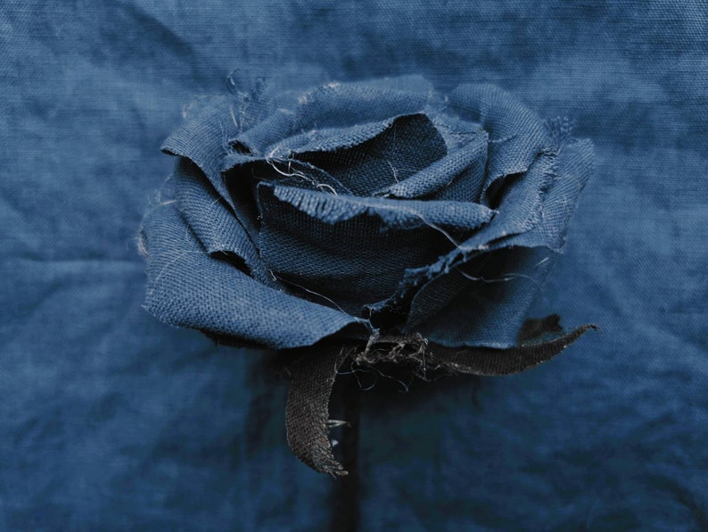 May include: A blue fabric rose with frayed edges, against a blue fabric background.