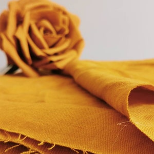 May include: A close-up of a folded piece of fabric in a rich mustard yellow color. The fabric has a soft, textured surface and is folded in a way that creates a gentle curve.