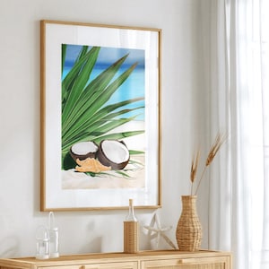 Peut inclure: Une impression encadrée d'une scène de plage tropicale avec des feuilles de palmier et des noix de coco. L'impression est dans un cadre en bois clair et est accrochée à un mur blanc.
