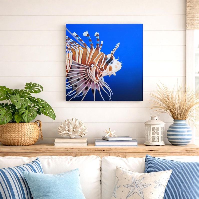 Tableau poisson lion peinture marine réaliste accroché au mur dans un salon style bord de mer avec décoration côtière et coussins bleus.
