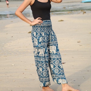 May include: A woman wearing a black tank top and blue and white patterned pants with an elephant design. The pants are loose fitting and have a wide leg.