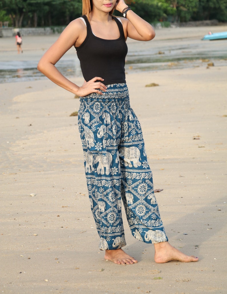 May include: A woman wearing a black tank top and blue and white patterned pants with an elephant design. The pants are loose fitting and have a wide leg.