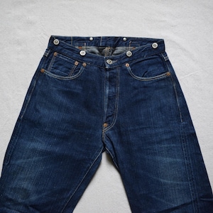May include: A pair of dark blue denim jeans with a button fly and a unique button closure at the waist.