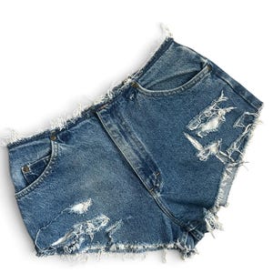 Peut inclure: Short en jean bleu à taille haute présentant une finition usée avec des bords effilochés et des détails déchirés sur les panneaux avant. Le vêtement comprend une fermeture à boutons classique, deux poches avant et une texture en jean bleu délavé.