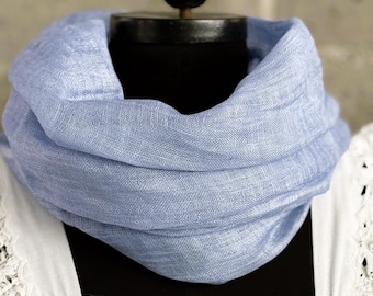 May include: A light blue scarf draped around a black mannequin head. The scarf is made of a lightweight fabric and has a soft, textured appearance. The background is a neutral color, highlighting the scarf's color and texture.
