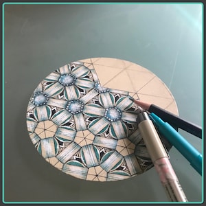 May include: A close-up of a circular piece of paper with a detailed black and white geometric design. The design features a repeating pattern of flowers with blue and green accents. Three drawing tools are visible on the right side of the image.