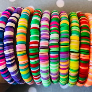 May include: A set of colourful bracelets made of stacked, round, flat, plastic beads. The bracelets are in various colours, including pink, blue, green, yellow, orange, and white.