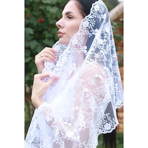 Puede incluir: Velo de encaje blanco con bordado floral. El velo es transparente y delicado, con un borde festoneado.