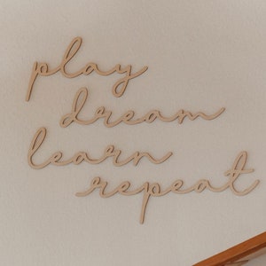 Puede incluir: Decoraci&oacute;n de pared de madera con las palabras "play dream learn repeat" en una fuente cursiva.