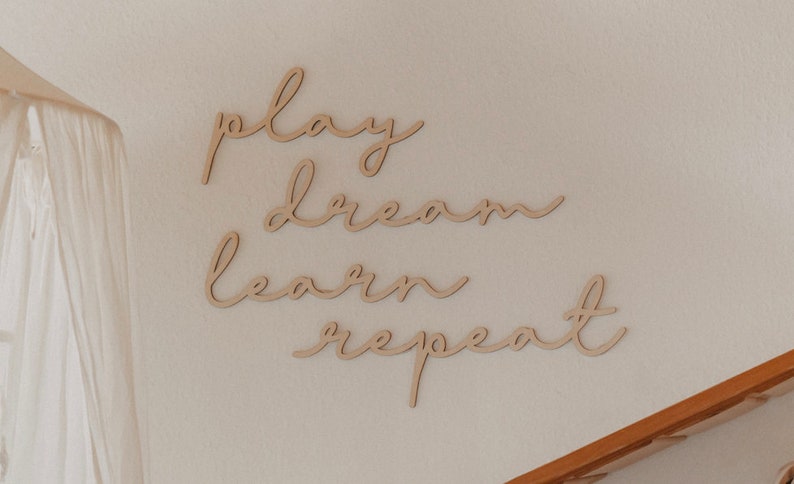 Puede incluir: Decoraci&oacute;n de pared de madera con las palabras "play dream learn repeat" en una fuente cursiva.