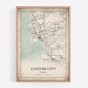 May include: Framed map print featuring a city map with roads, water, and green areas. The map is in a vintage style with a light brown frame. Text at the bottom reads "CUSTOM CITY" and coordinates.