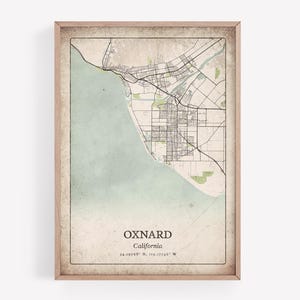 Może przedstawiać: Oprawiony wydruk mapy w stylu vintage z Oxnard, Kalifornia, z szczegółowym układem ulic, obszarami przybrzeżnymi i terenami zielonymi. Mapa ma jasnobrązową ramę i zawiera nazwę miasta i współrzędne.