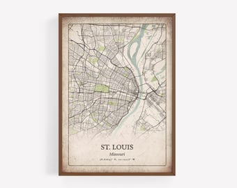 May include: Framed map print of St. Louis, Missouri, with a vintage aesthetic. The map features a detailed street layout, green park areas, and a light blue river. The text "ST. LOUIS" and coordinates are printed at the bottom.