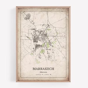 May include: Framed map print of Marrakech, Morocco. The map shows a detailed street layout in black and grey, with green areas for parks. The city name and coordinates are printed at the bottom. The frame is a light brown colour.