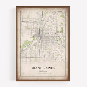 May include: A framed map print of Grand Rapids, Michigan, with a vintage aesthetic. The map shows a detailed street grid, with green areas representing parks and waterways. The city name and coordinates are printed at the bottom, framed in a brown wooden frame.