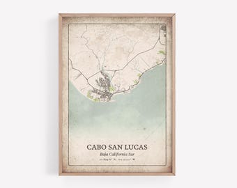 May include: A framed map print of Cabo San Lucas, Baja California Sur. The map features a detailed illustration of the city's layout, with roads, buildings, and coastal features. The print has a vintage aesthetic with a light brown frame and a faded color palette.