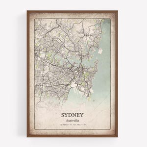 May include: A framed map print of Sydney, Australia, in a vintage style. The map features detailed street layouts and geographical features, with a light green and beige color scheme. The city name and coordinates are printed at the bottom.