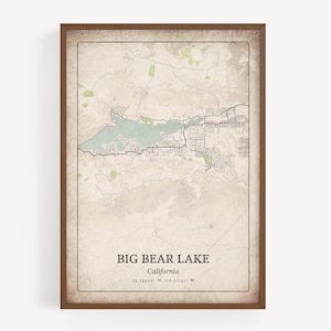 May include: A framed map print of Big Bear Lake, California, with a vintage aesthetic. The map features a light blue lake, green areas, and black roads, set against a beige background. The text "BIG BEAR LAKE California" is displayed at the bottom.