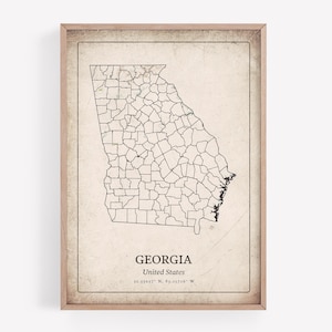 May include: A framed vintage-style map of Georgia, United States, with county lines in black. The map is set against a beige background with the state's name and coordinates at the bottom. The frame is a light brown color.