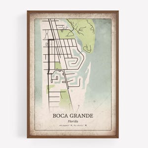 May include: Framed vintage-style map print of Boca Grande, Florida, featuring a detailed street layout in black against a faded green and blue background. The print includes the location's name and coordinates.