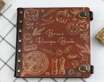 May include: A brown leather-bound recipe book with a gold engraved design of various food items, including pizza, peppers, and herbs. The book has the text "Bree's Recipe Book" engraved on the front cover.
