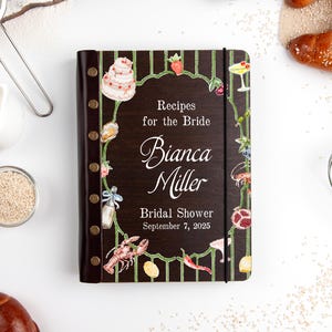 Puede incluir: Un libro de recetas marrón oscuro con el texto "Recipes for the Bride" y el nombre "Bianca Miller". La portada está decorada con ilustraciones de alimentos y un borde floral. La fecha de la despedida de soltera es el 7 de septiembre de 2025.