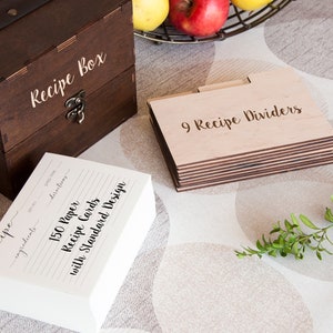 Peut inclure: Une bo&icirc;te &agrave; recettes en bois fonc&eacute; avec le texte "Recipe Box" et un fermoir en m&eacute;tal. &Agrave; c&ocirc;t&eacute;, une pile de 150 fiches de recettes en papier et 9 s&eacute;parateurs de recettes en bois. Les fiches ont des lignes pour les ingr&eacute;dients et les instructions.