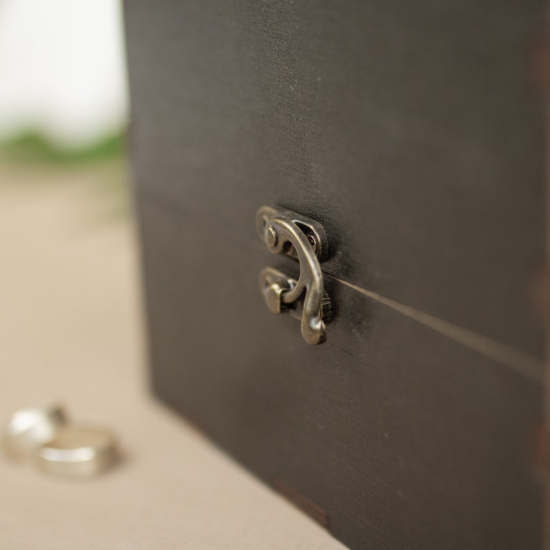 May include: A black wooden box with a metal latch. The latch is ornate and has a decorative design.