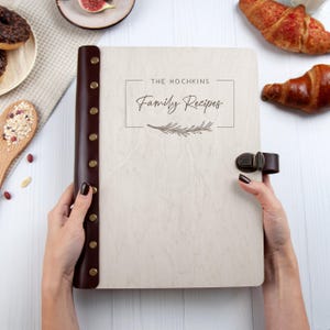 May include: A white wooden recipe book with a brown leather spine and a brass clasp. The book has the text "THE HOCHKINS Family Recipes" engraved on the front cover.