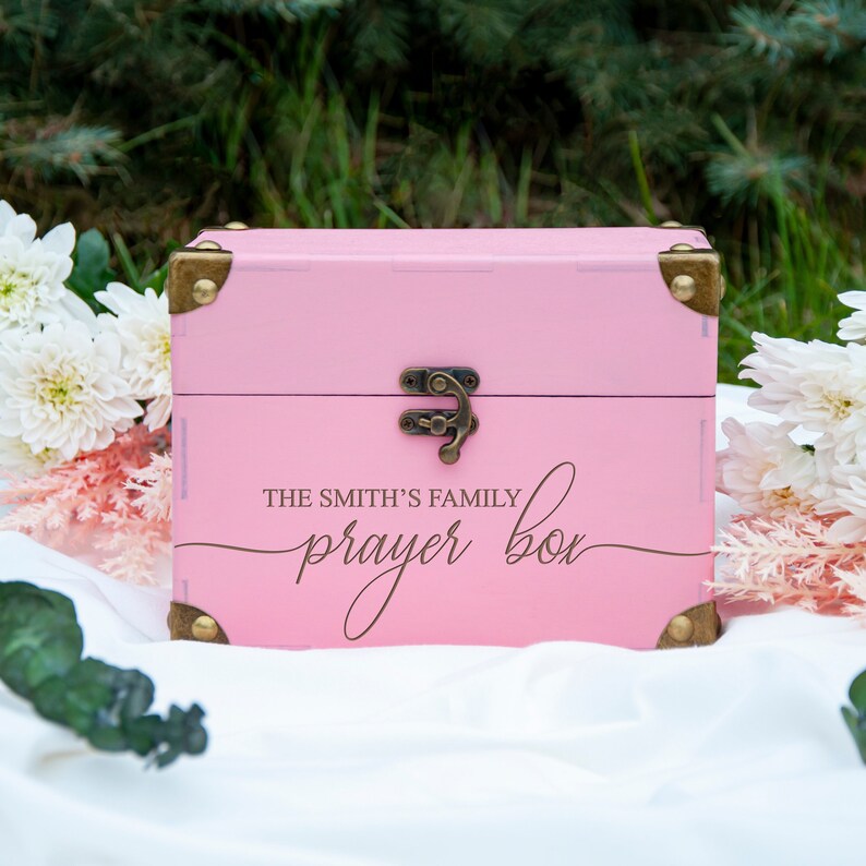 May include: A pink wooden box with a brass latch and hinges. The box has the text "The Smith's Family Prayer Box" written on the front in a cursive font.