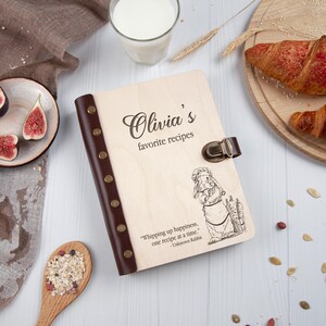 May include: A wooden recipe book with a brown leather cover and a quote about whipping up happiness. The book is engraved with the text "Olivia's favourite recipes" and a cartoon rabbit wearing a chef's hat.