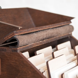 May include: A wooden box with a hinged lid and a felt lining. The box has multiple slots for holding cards or other small items.