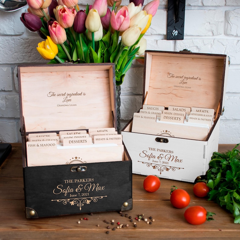 May include: Two wooden recipe boxes, one black and one white, with engraved text. The black box reads "The Parkers Sofia & Max June 7, 2021." The white box has the same text. Both boxes have dividers labeled for different recipe categories.