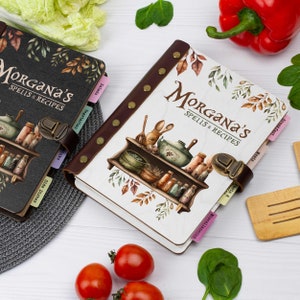 Pu&ograve; includere: Due libri di ricette in bianco e nero con il titolo "Morgana's Spells & Recipes" e un'illustrazione colorata di uno scaffale da cucina con varie bottiglie e barattoli. I libri hanno schede per diverse categorie, tra cui "Colazione", "Carne", "Pasta e piatti principali", "Insalate", "Vegetariano", "Contorni" e "Varie".