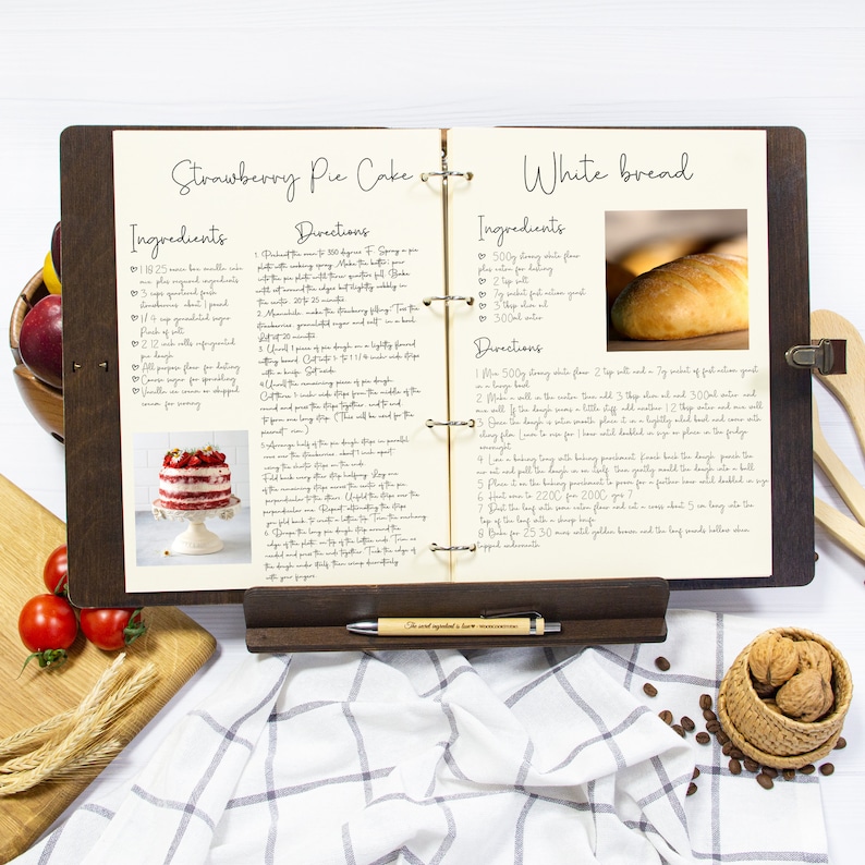 May include: Open recipe book with two pages showing recipes for Strawberry Pie Cake and White Bread. The Strawberry Pie Cake recipe includes ingredients like sponge cake, strawberries, and whipped cream. The White Bread recipe includes ingredients like flour, yeast, and water.