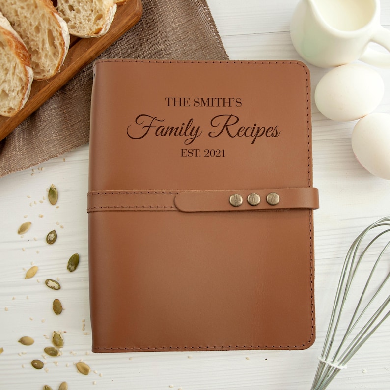 May include: A brown leather recipe book with the text "The Smith's Family Recipes Est. 2021" embossed on the front cover.